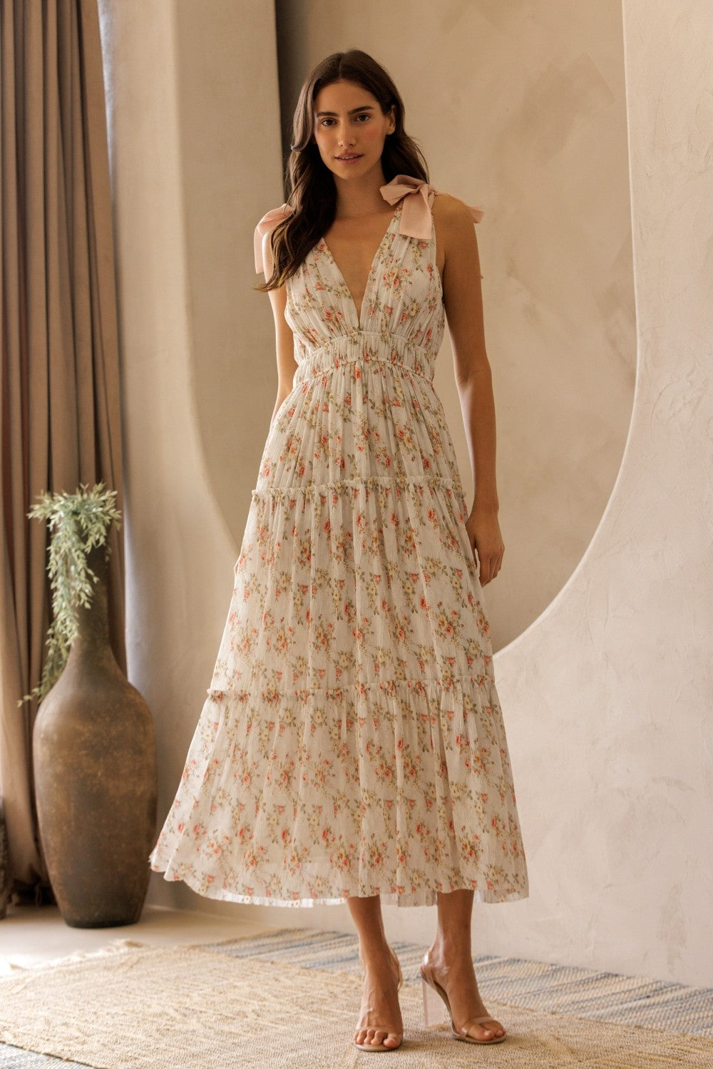 woman wearing a floral maxi dress with tie straps and a tiered skirt, standing against a neutral background