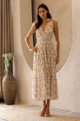 woman wearing a floral print sleeveless maxi dress with tie detail on shoulders, standing indoors