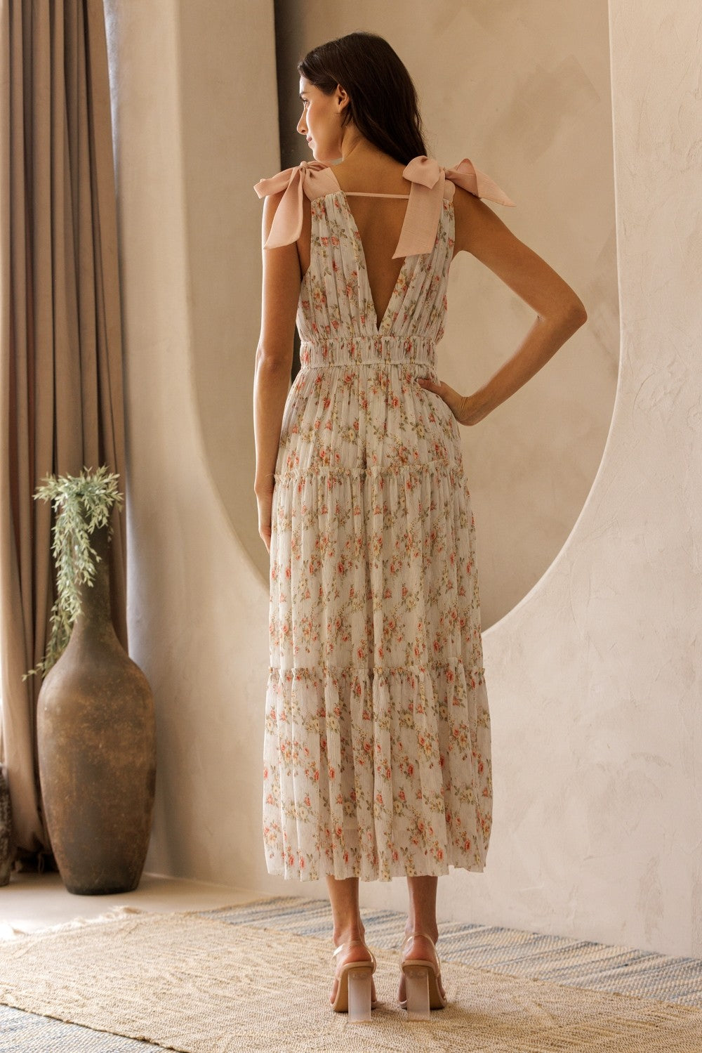 woman wearing a floral midi dress with a v-back and tie straps, standing with her back to the camera