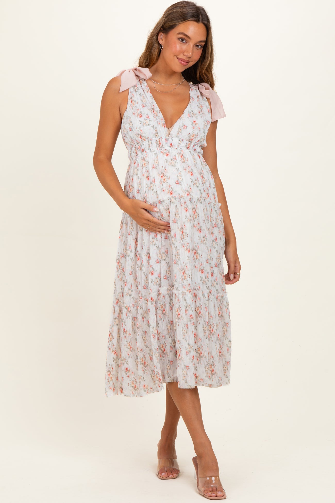 woman wearing a floral maternity maxi dress with bow tie straps and holding her baby bump
