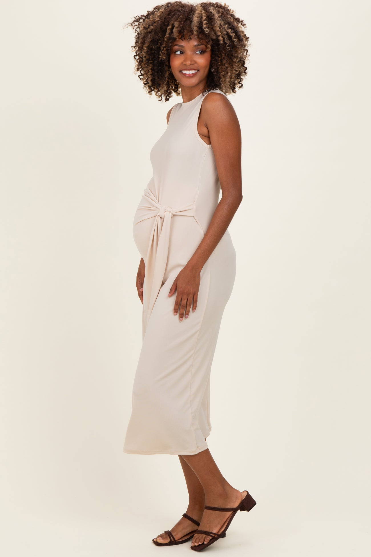woman wearing a beige midi maternity dress with a side knot detail and a visible baby bump