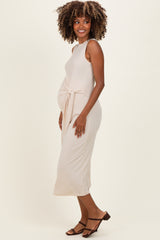 woman wearing a beige midi maternity dress with a side knot detail and a visible baby bump