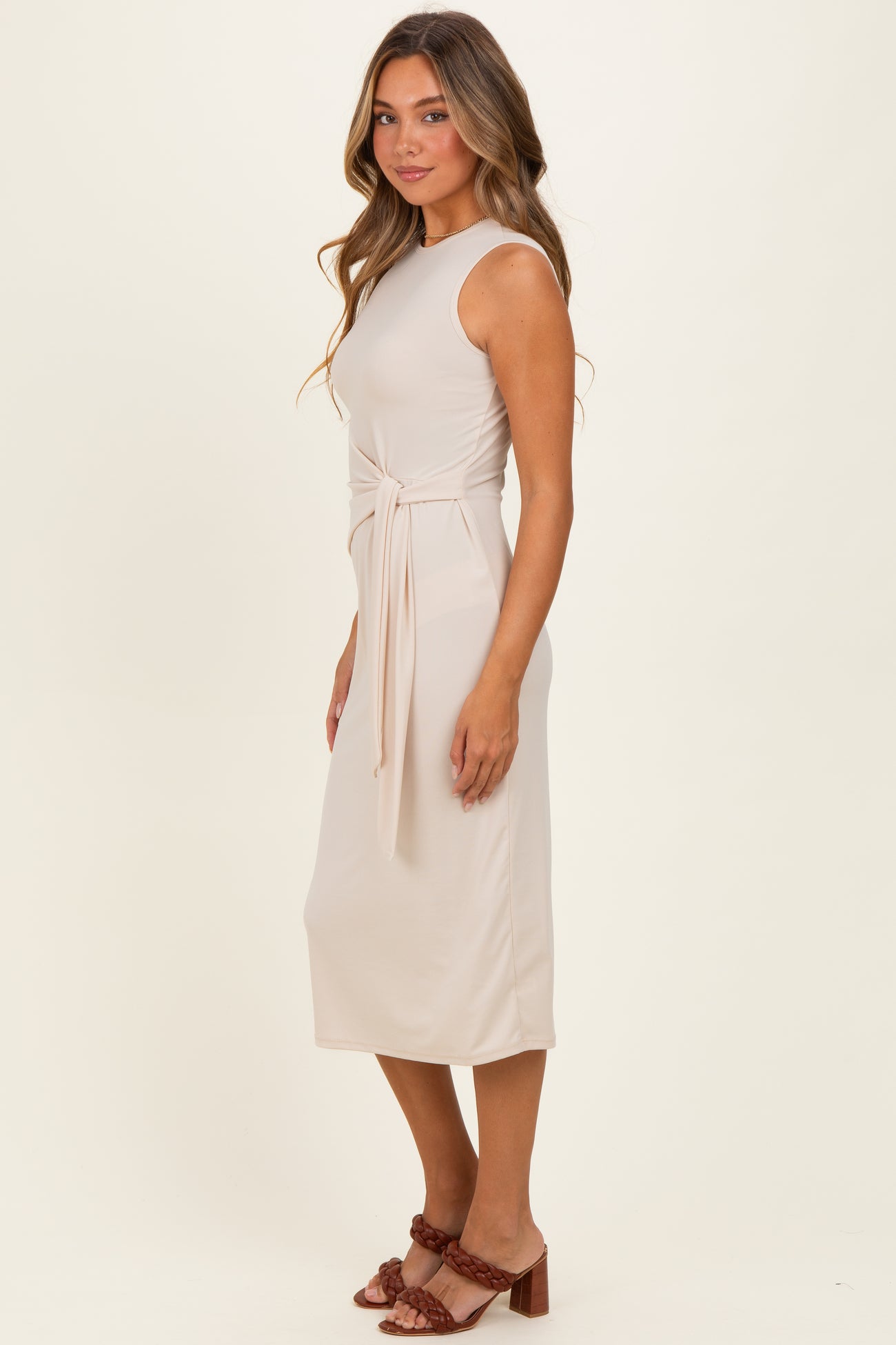 woman wearing a fitted beige midi dress with a tied waist detail and a scoop neckline