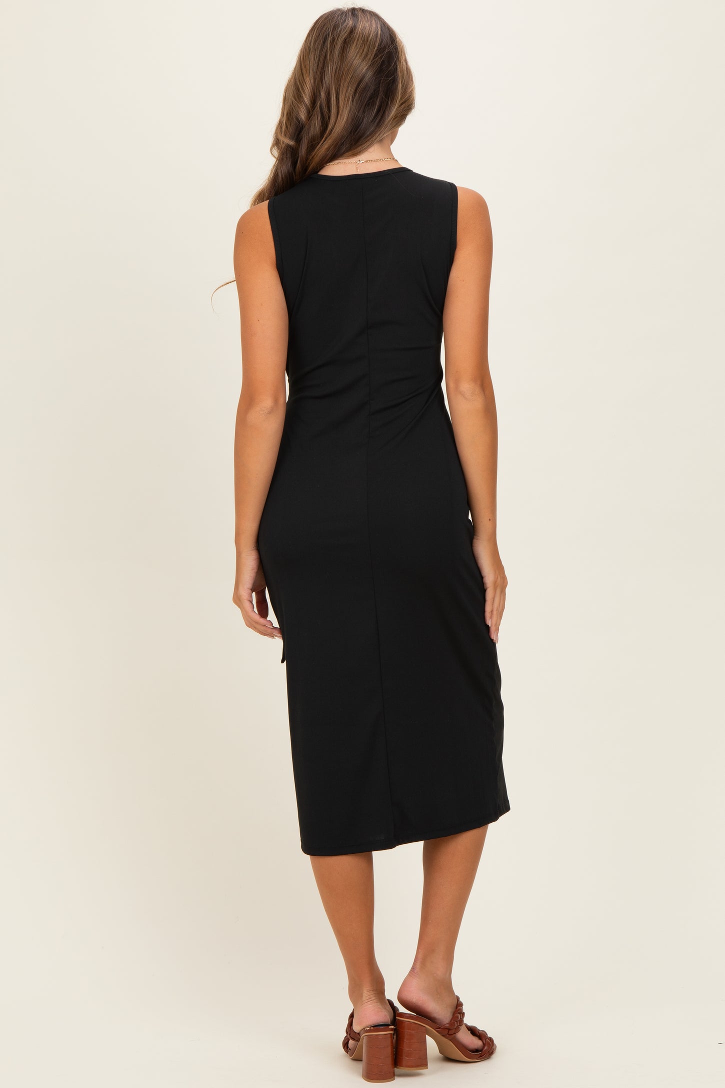 woman wearing a black sleeveless midi dress, showing the back view and styled with brown sandals