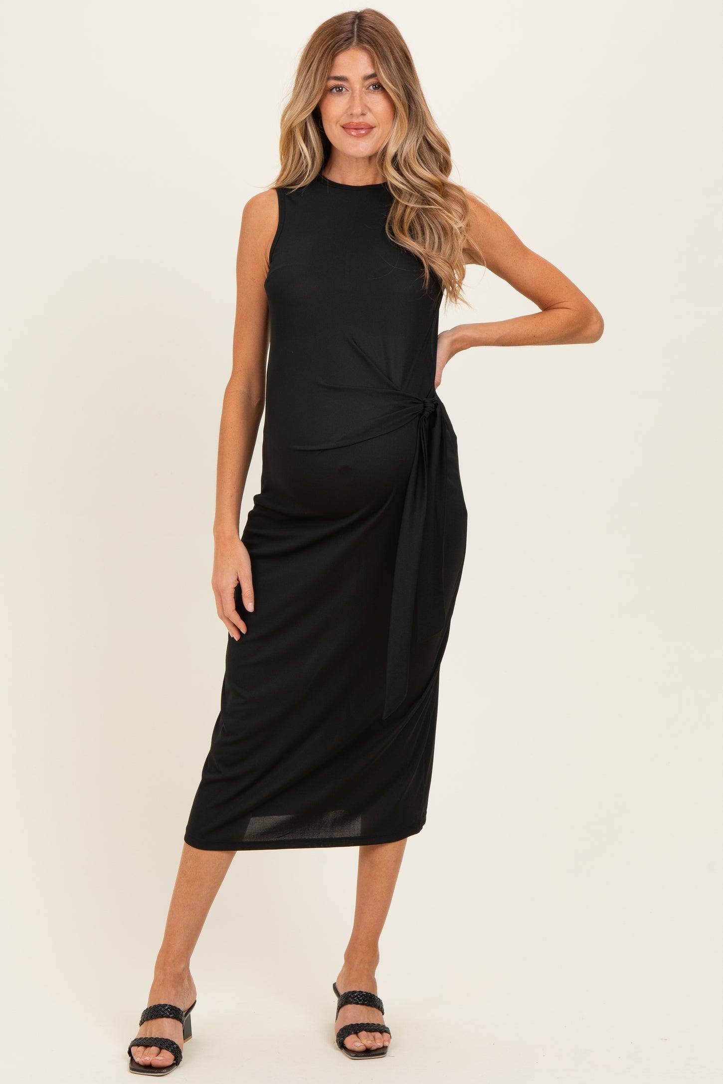 woman wearing a black sleeveless maternity midi dress with a side tie and a visible baby bump