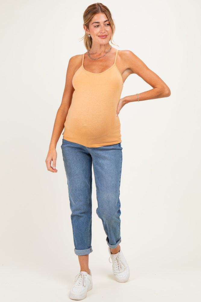 woman wearing a light orange maternity tank top and blue jeans, showcasing her baby bump