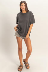 woman wearing an oversized charcoal gray t-shirt with distressed denim shorts and brown sandals