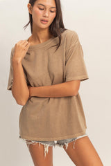 woman wearing a loose-fitting brown oversized t-shirt with rolled sleeves and distressed denim shorts