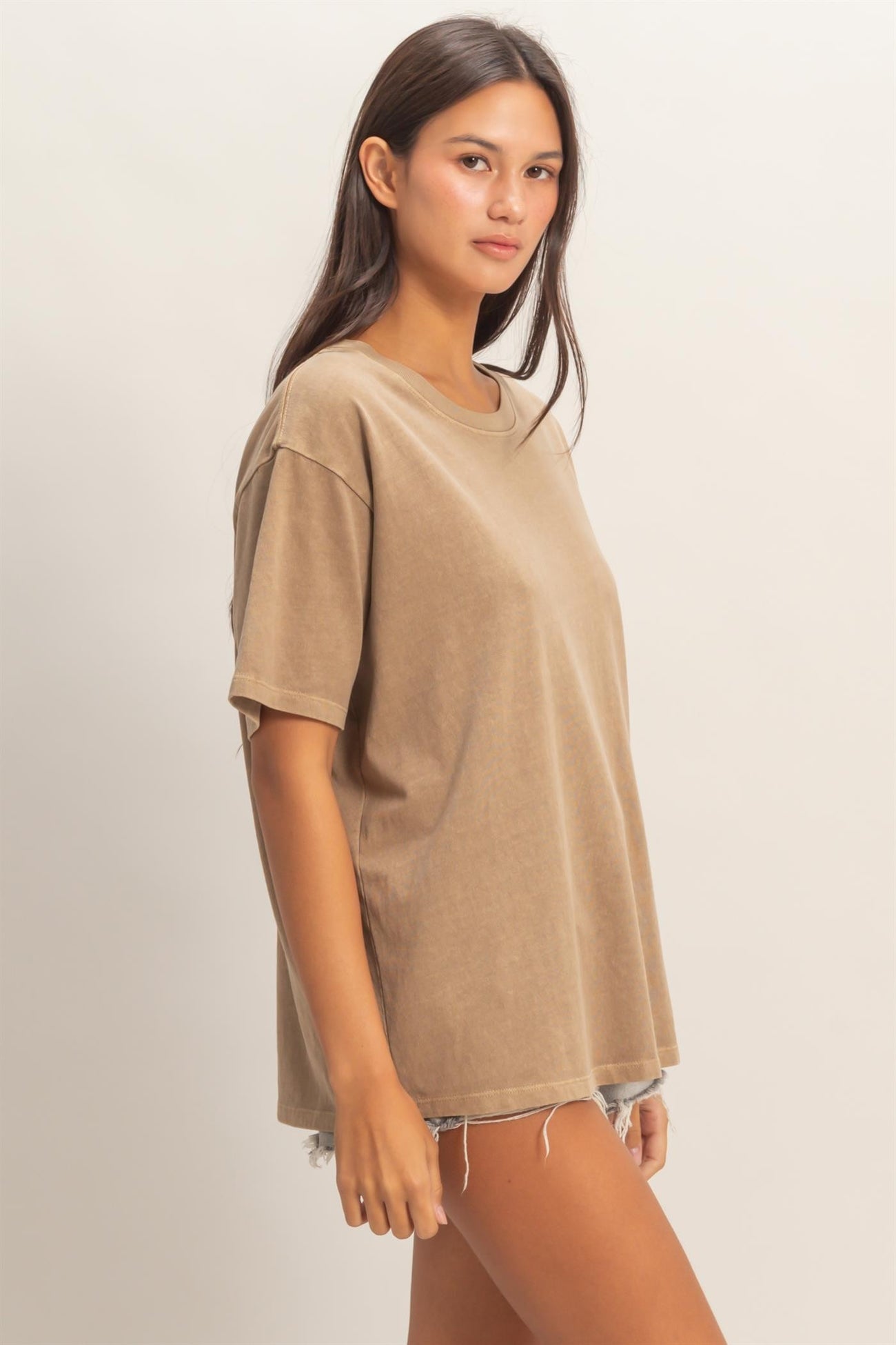 woman wearing a loose-fitting tan oversized t-shirt paired with distressed denim shorts