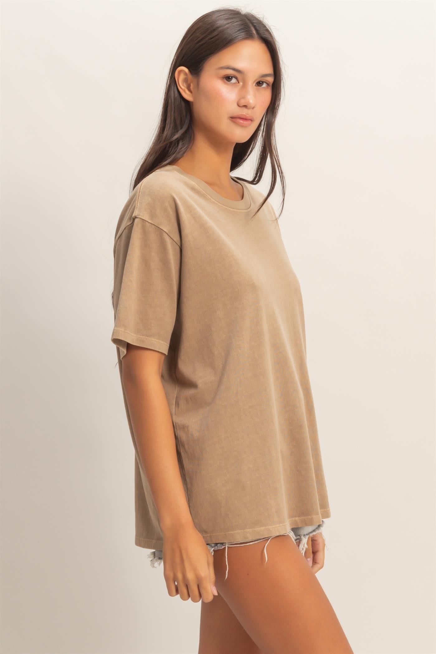 woman wearing a loose-fitting tan oversized t-shirt paired with distressed denim shorts