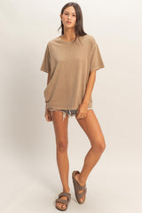 woman wearing a taupe oversized t-shirt with rolled sleeves and distressed denim shorts