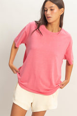 woman wearing a pink short sleeve t-shirt and light beige shorts, posing with hands on hips