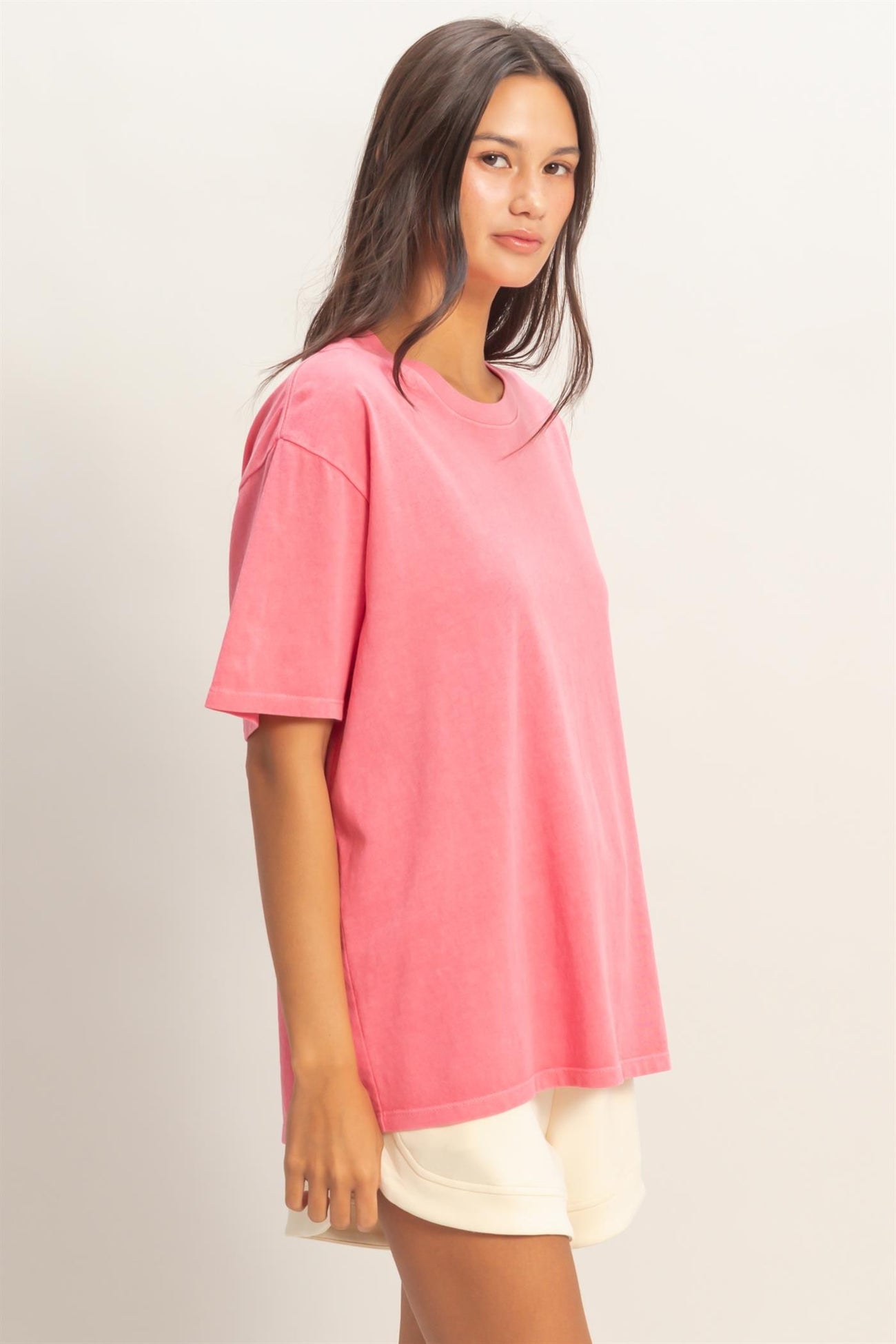 woman wearing a pink oversized t-shirt with short sleeves and a relaxed fit, styled with cream shorts