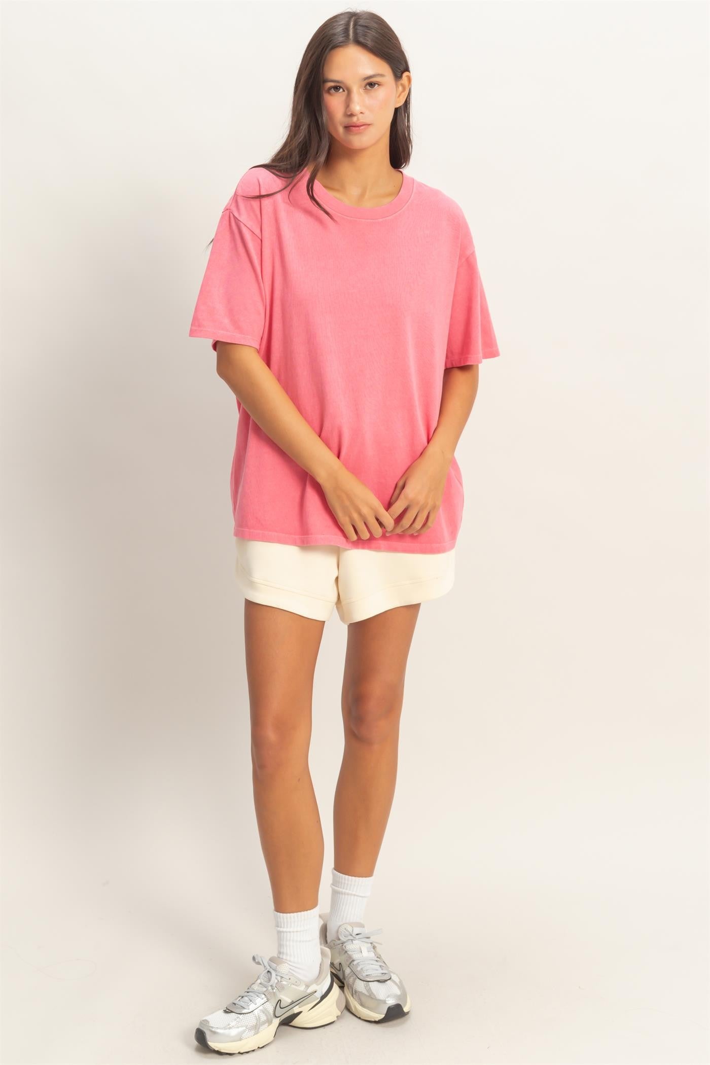woman wearing a pink oversized t-shirt and cream shorts with white socks and sneakers