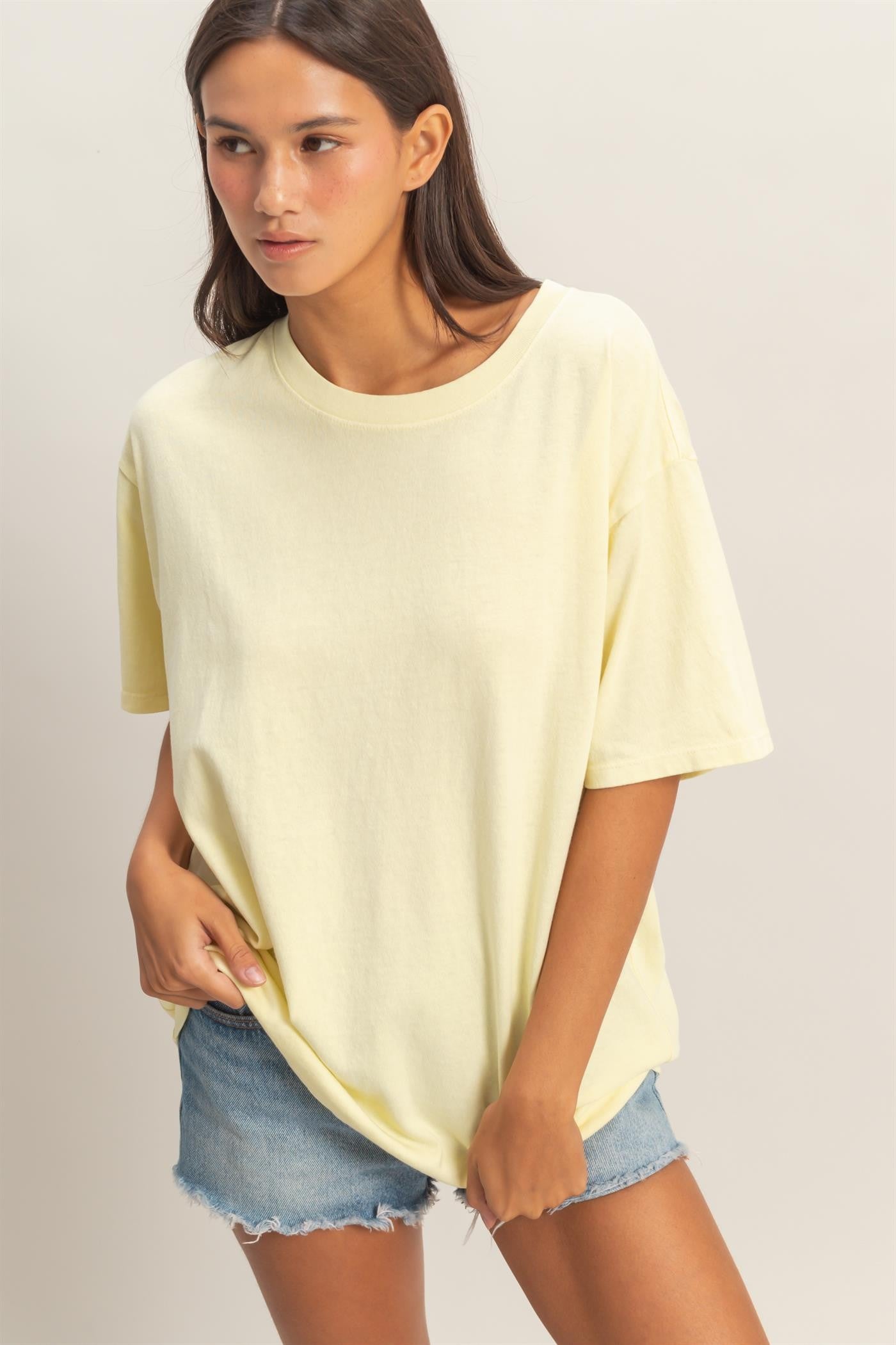 woman wearing a light yellow oversized t-shirt and distressed denim shorts