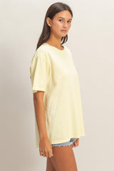 woman wearing a light yellow oversized t-shirt and distressed denim shorts, standing sideways with a relaxed pose