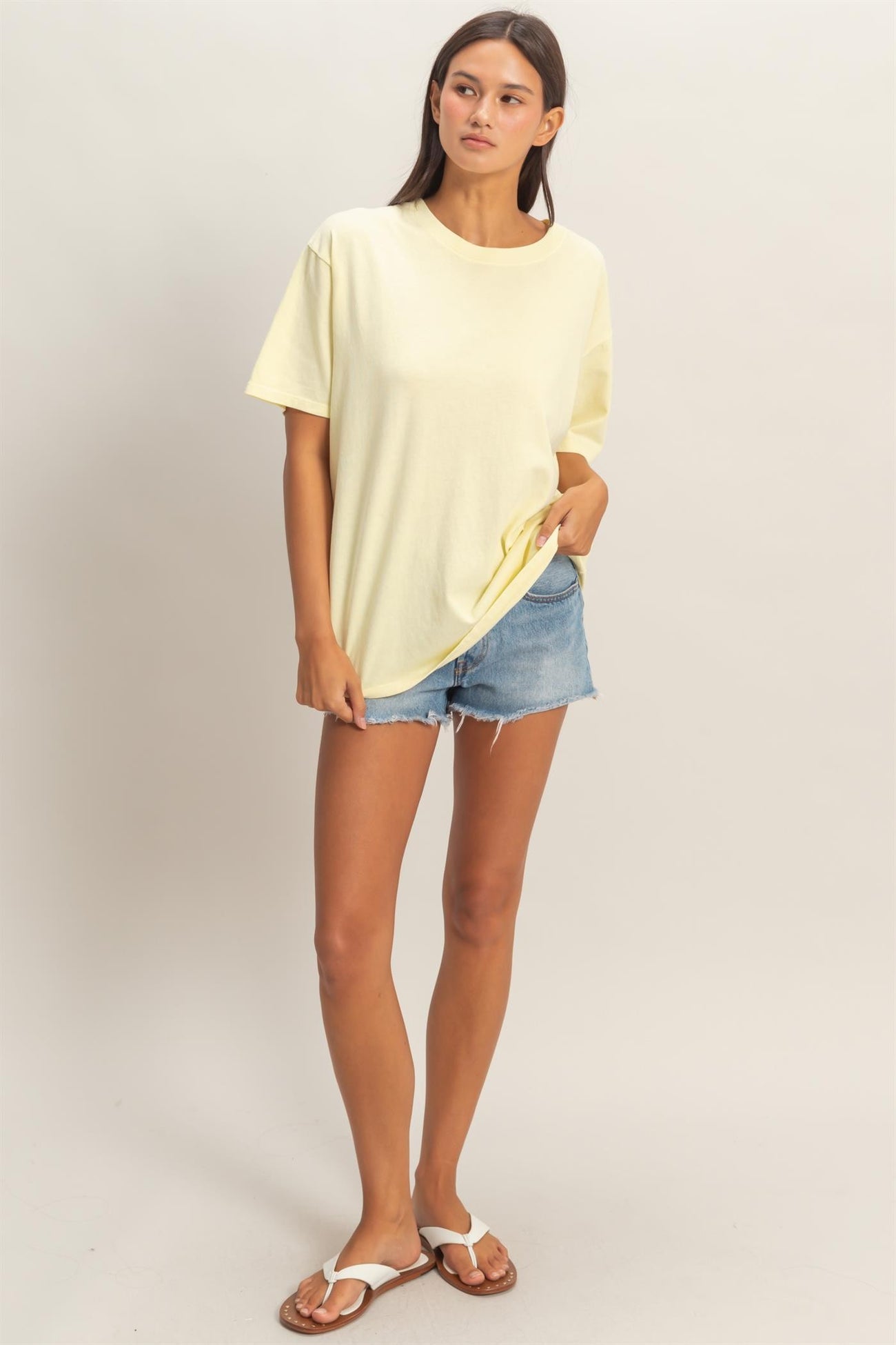 woman wearing a yellow oversized t-shirt and denim shorts, standing in a relaxed pose