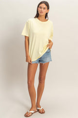 woman wearing a yellow oversized t-shirt and denim shorts, standing in a relaxed pose