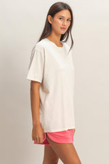 woman wearing a cream oversized t-shirt and pink athletic shorts, standing casually and looking at the camera