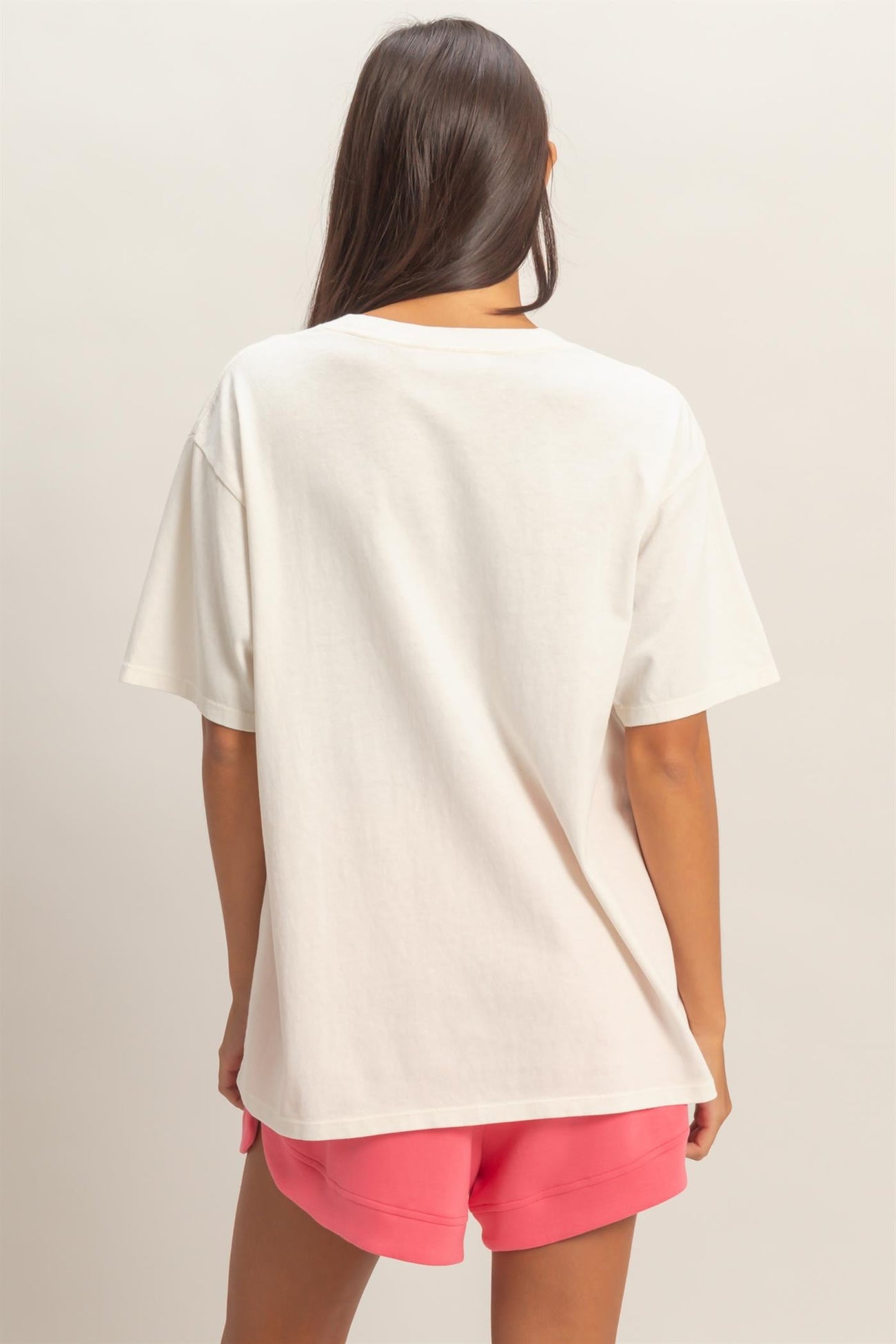 woman wearing an oversized cream t-shirt paired with pink athletic shorts, view from the back