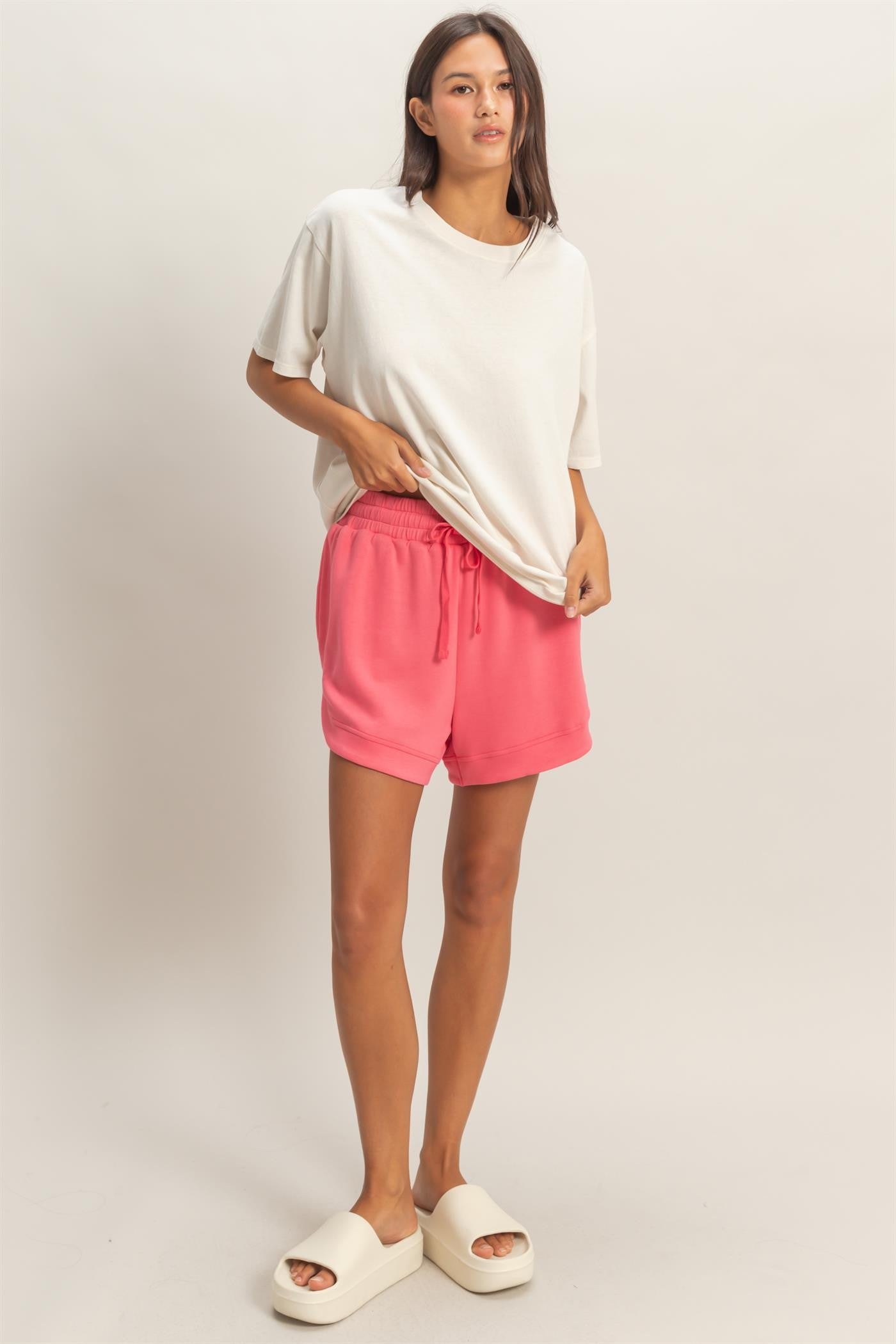 woman wearing a relaxed fit beige t-shirt and pink drawstring shorts, styled with white sandals