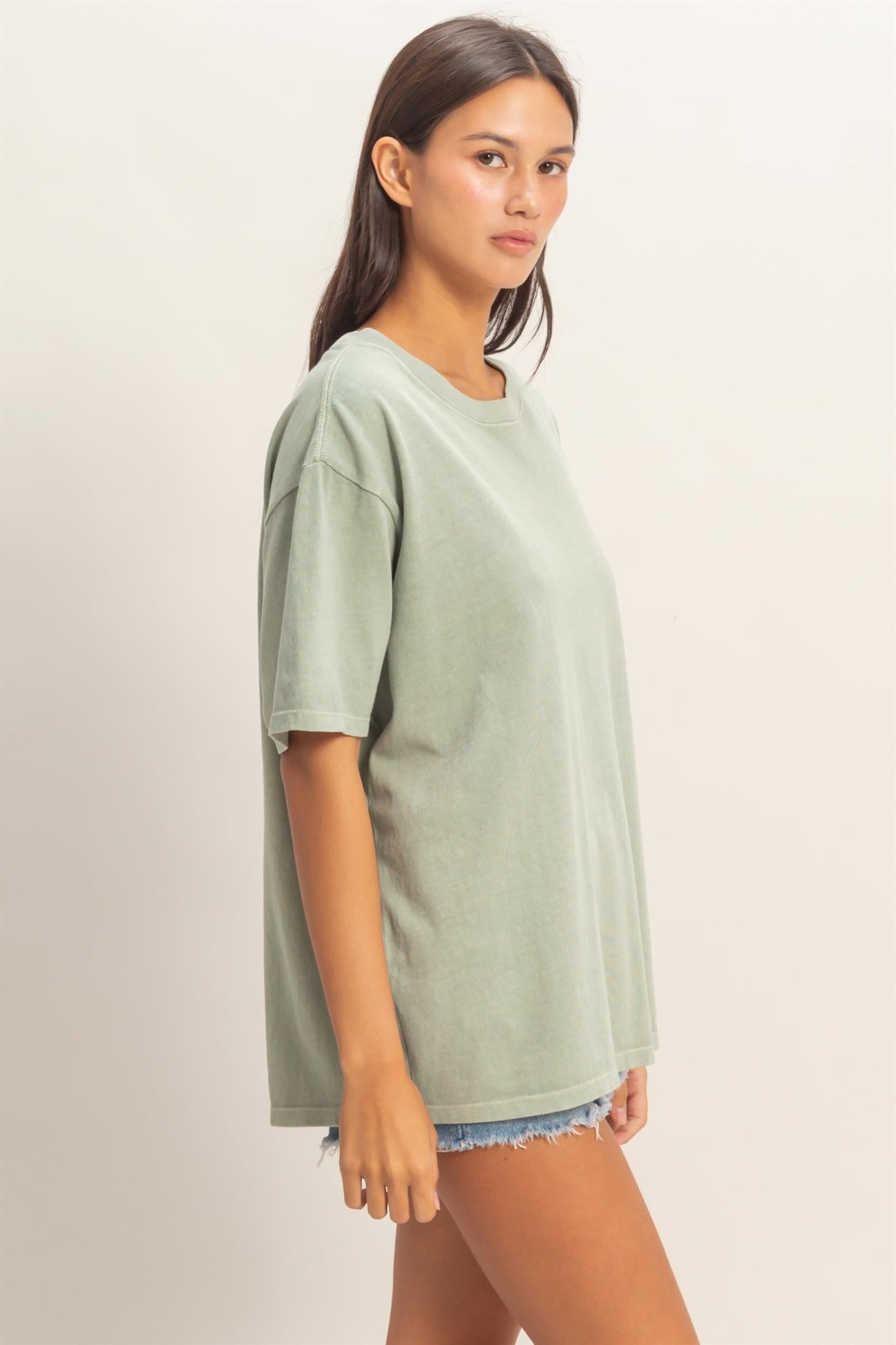 woman wearing a relaxed fit light green oversized t-shirt with short sleeves and distressed denim shorts