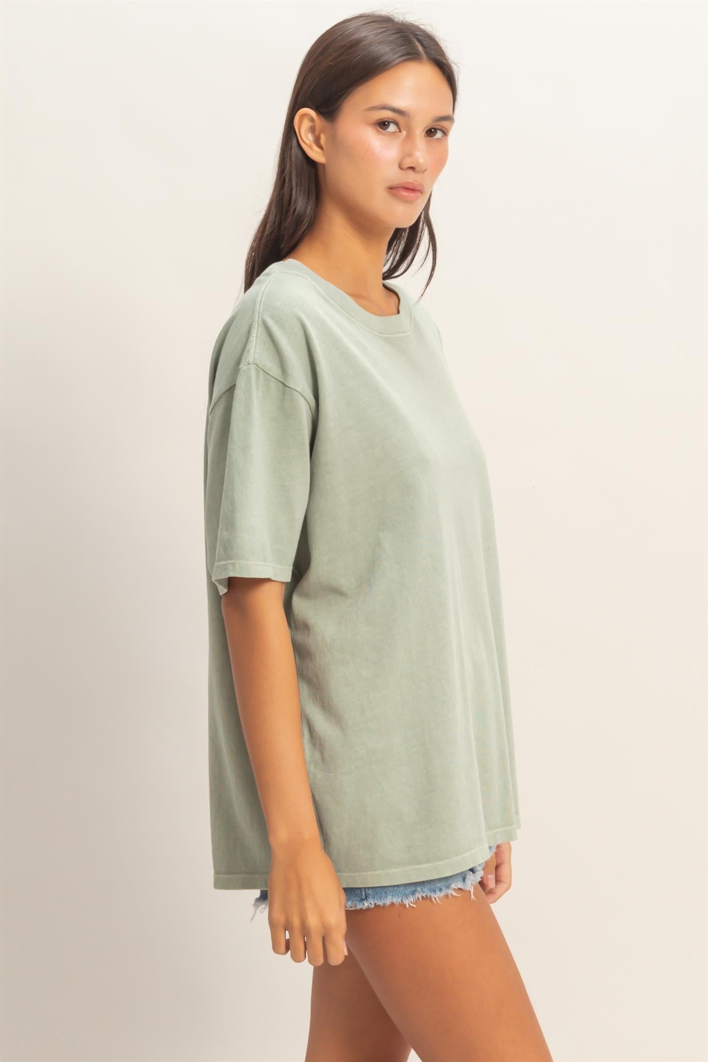 woman wearing a relaxed fit light green oversized t-shirt with short sleeves and distressed denim shorts