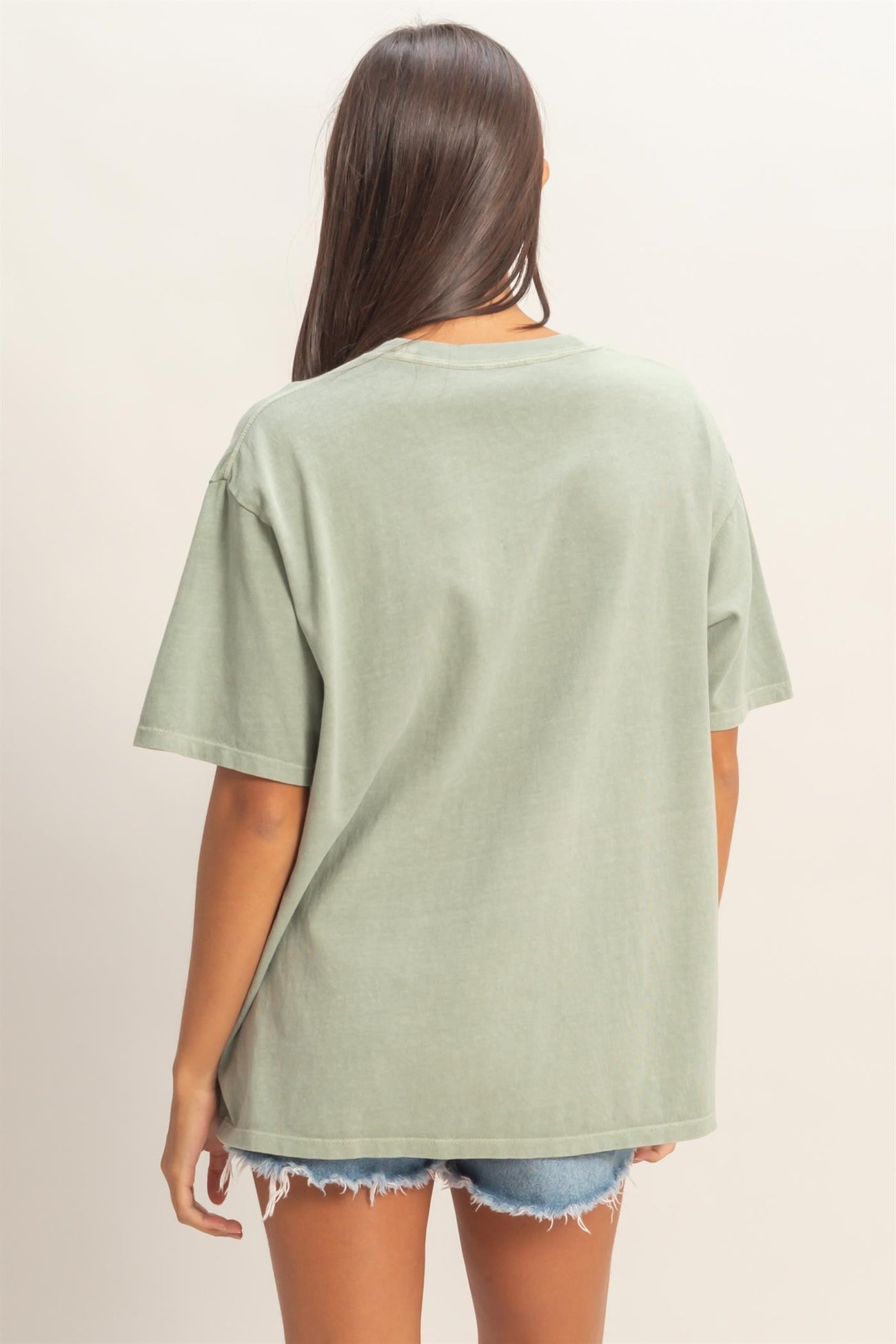 woman wearing a relaxed fit green oversized t-shirt with short sleeves and back view, paired with denim shorts