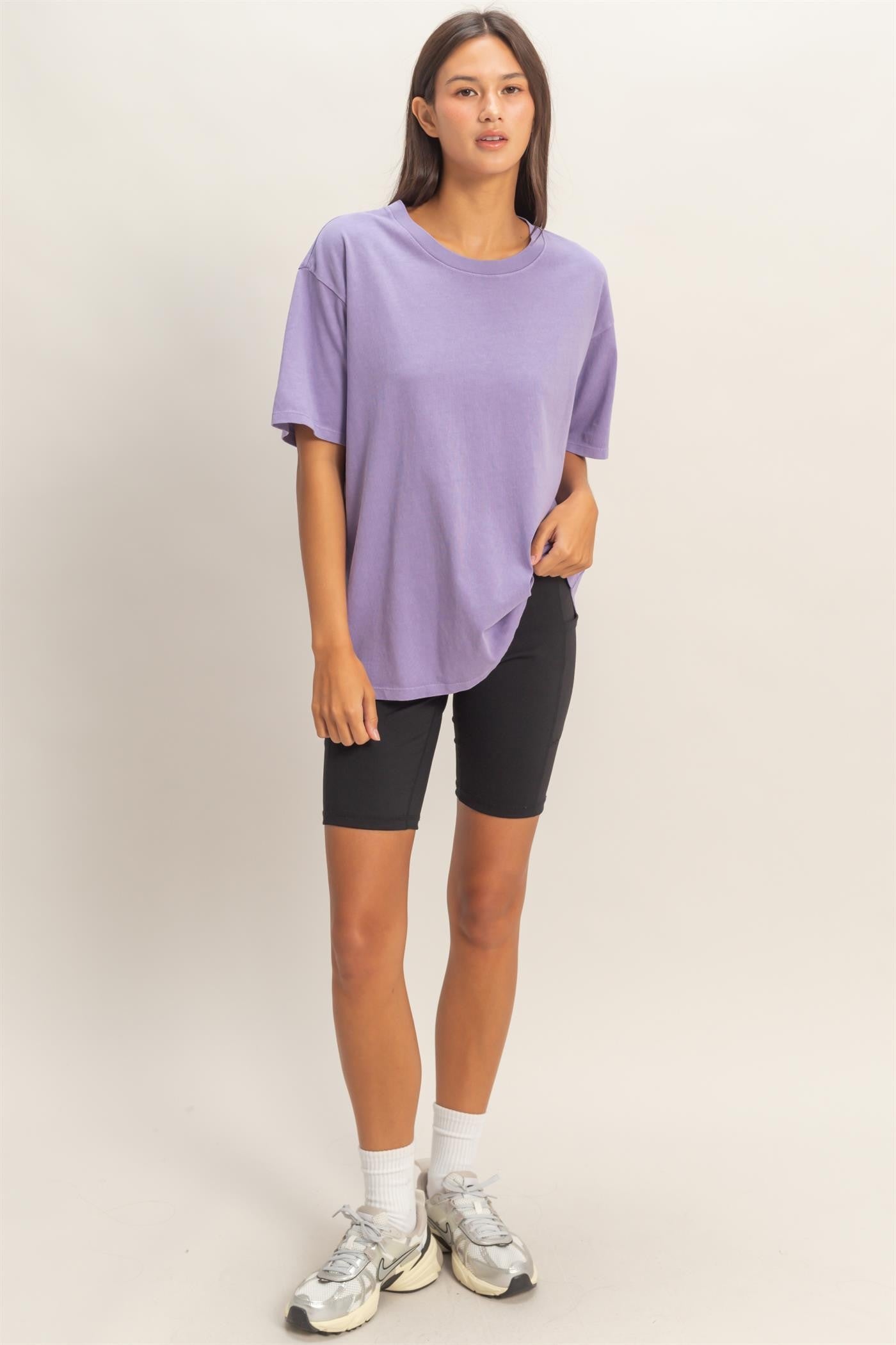 woman wearing a purple oversized t-shirt and black bike shorts with white socks and sneakers.
