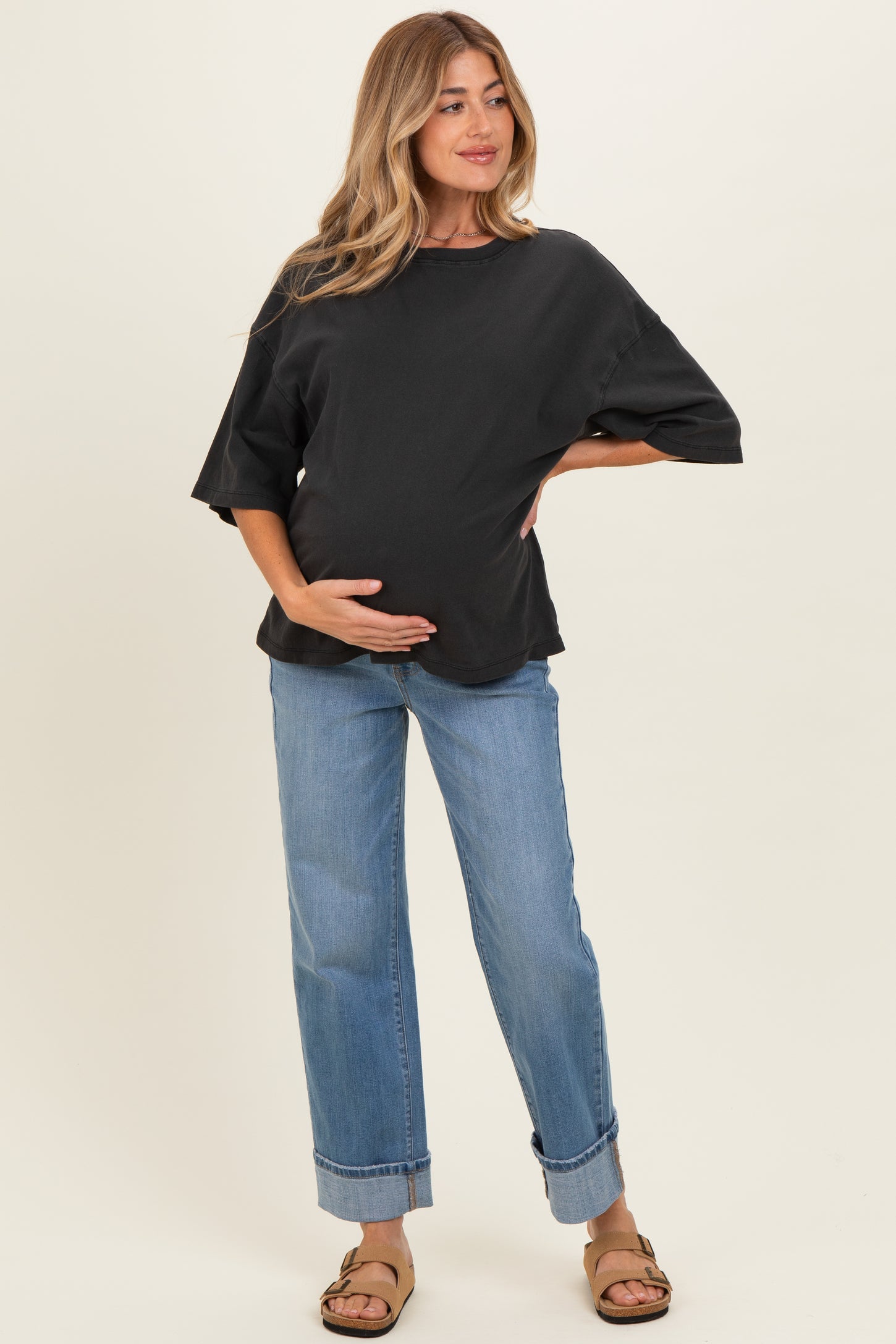 woman wearing a black oversized maternity top and light blue cuffed jeans, holding her baby bump