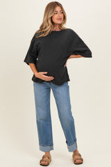 woman wearing a black oversized maternity top and light blue cuffed jeans, holding her baby bump