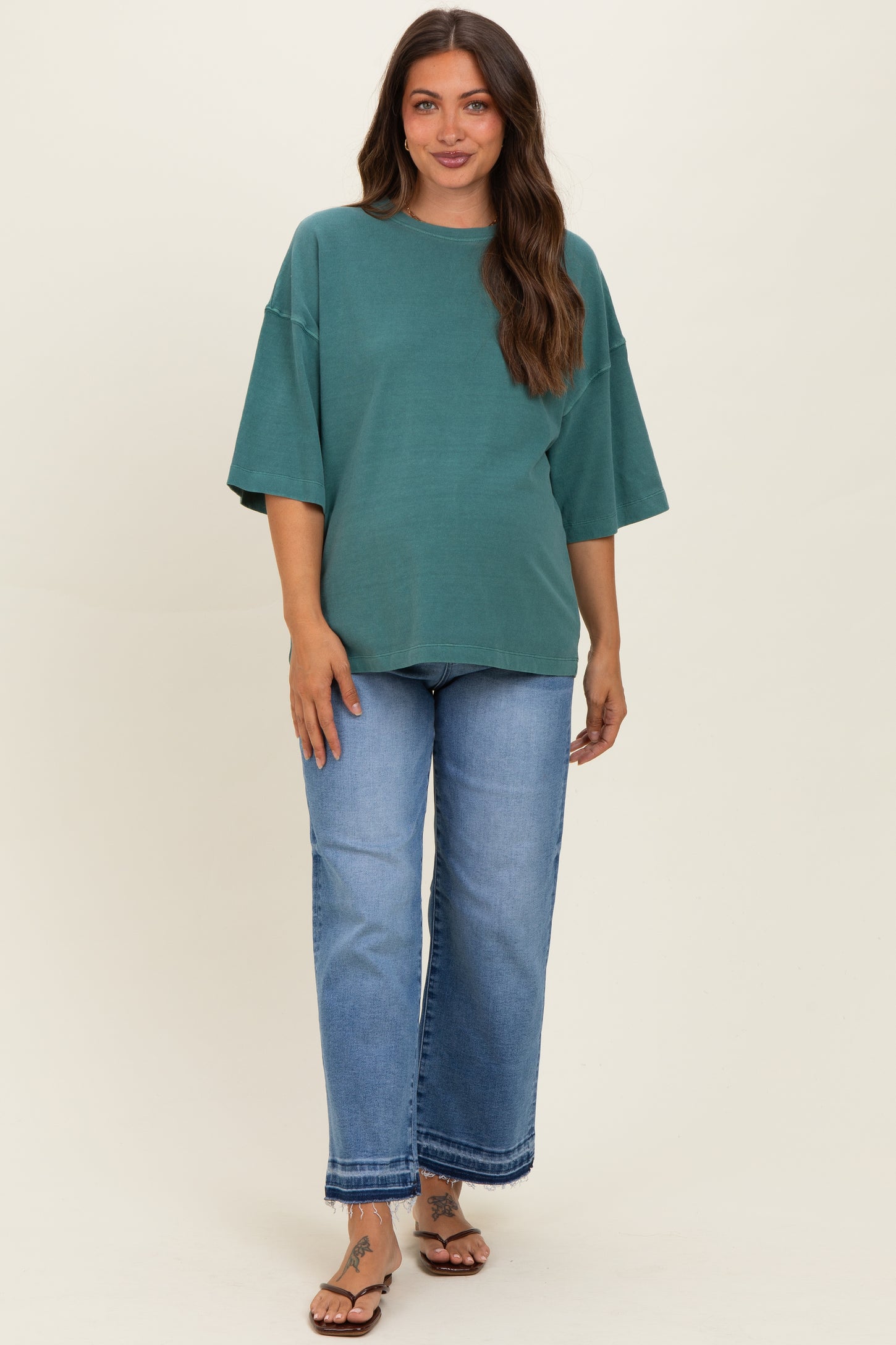 woman wearing a green oversized maternity t-shirt with short sleeves and blue wide-leg jeans