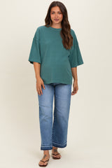 woman wearing a green oversized maternity t-shirt with short sleeves and blue wide-leg jeans