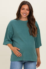 woman wearing a teal maternity top with short sleeves and holding her baby bump