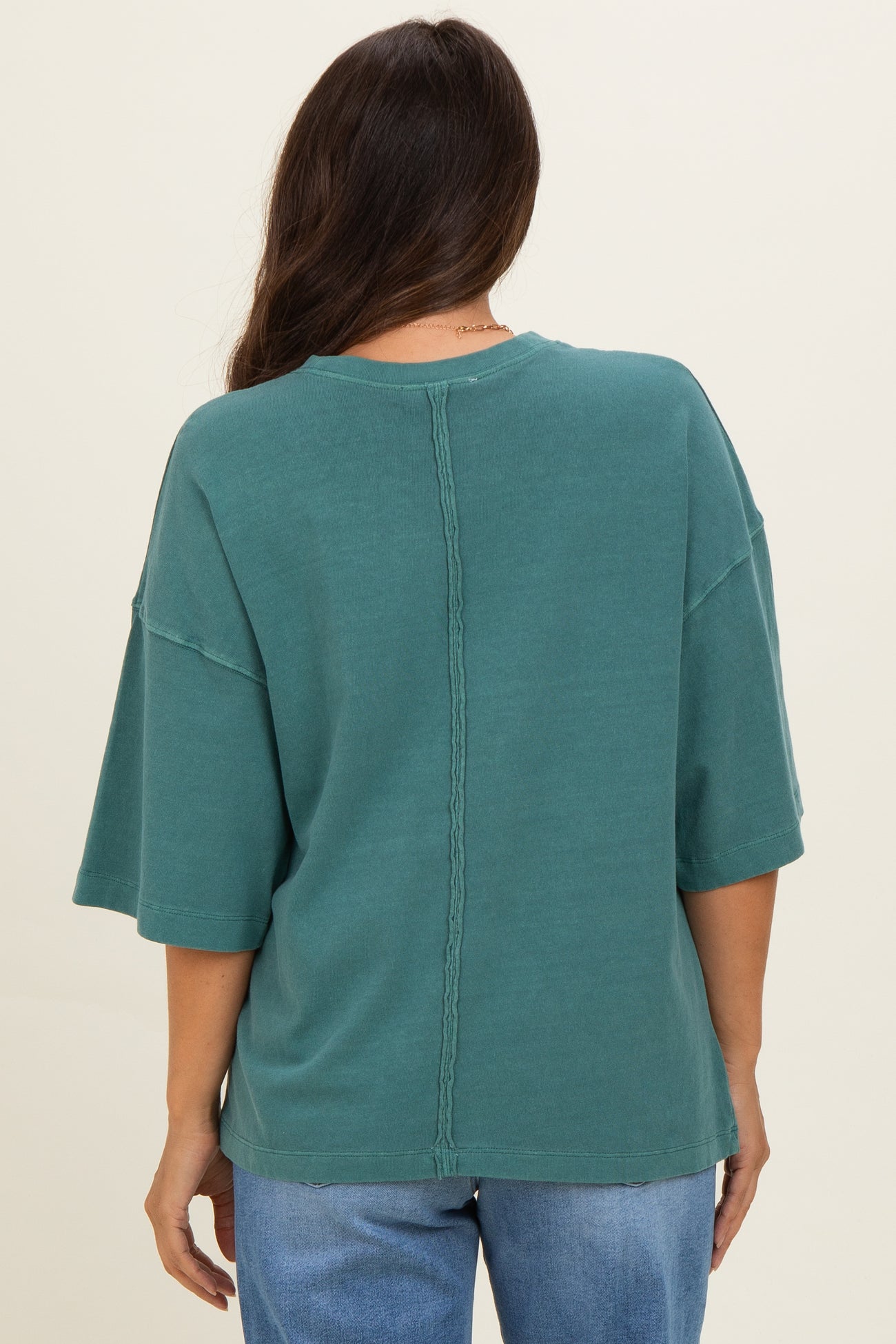 woman wearing a teal oversized maternity top with short sleeves and a stylish back seam detail