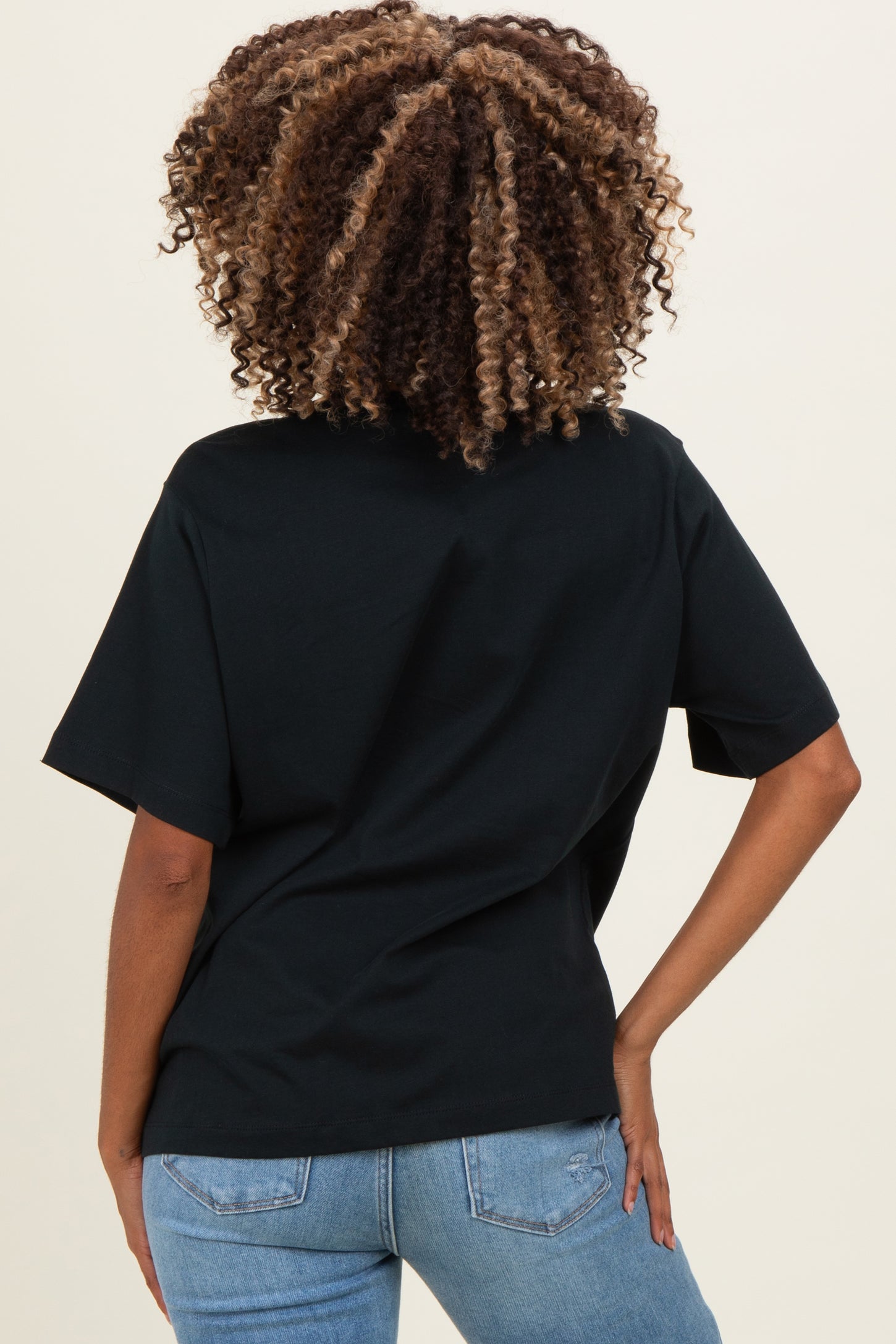 woman wearing a black short sleeve maternity top and blue jeans, showing her back and curly hair