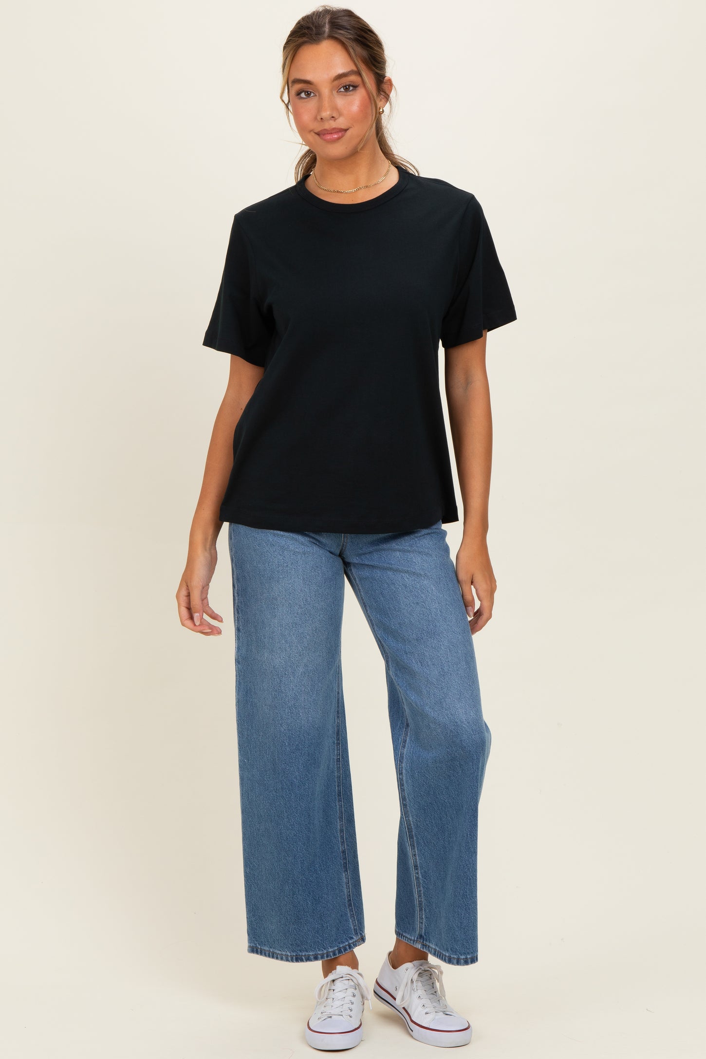 woman wearing a black oversized t-shirt with short sleeves and high-waisted wide-leg jeans, paired with white sneakers