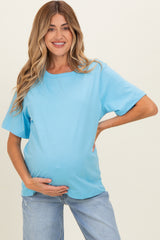 woman wearing a light blue maternity top and holding her baby bump, styled with casual denim jeans