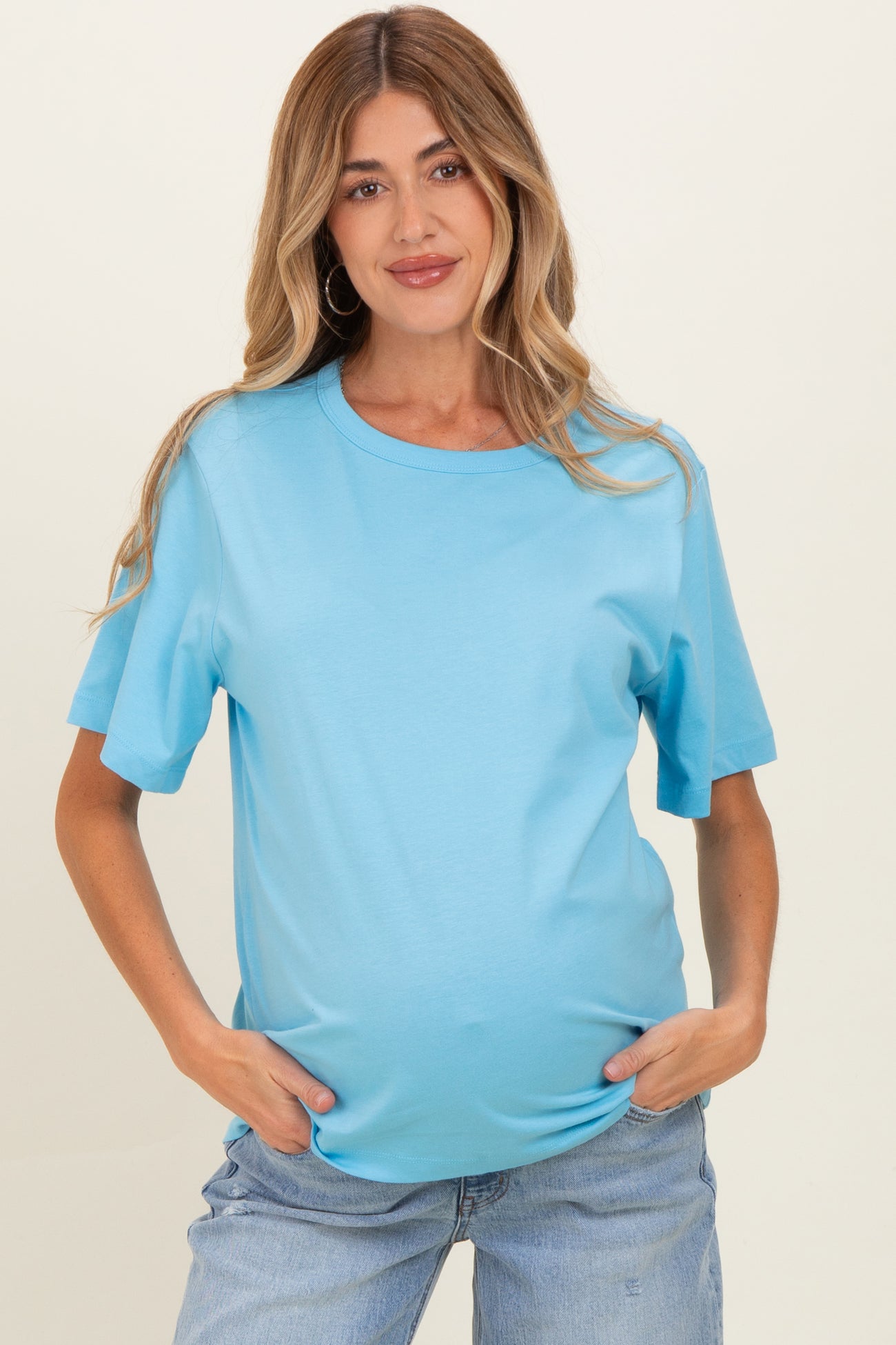 woman wearing a light blue short sleeve maternity top with a visible baby bump and relaxed jeans