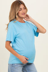 woman wearing a light blue short sleeve maternity top and showcasing her baby bump