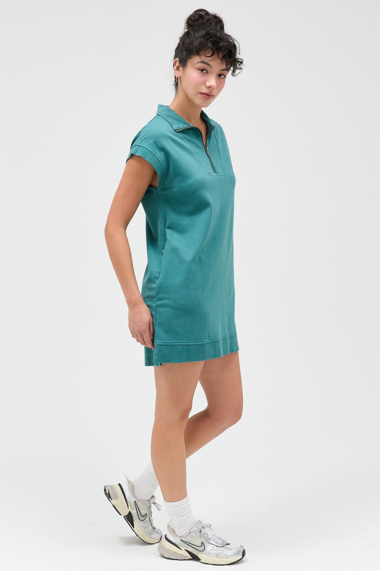 woman wearing a teal polo dress with a zipper collar and rolled sleeves, styled with sneakers