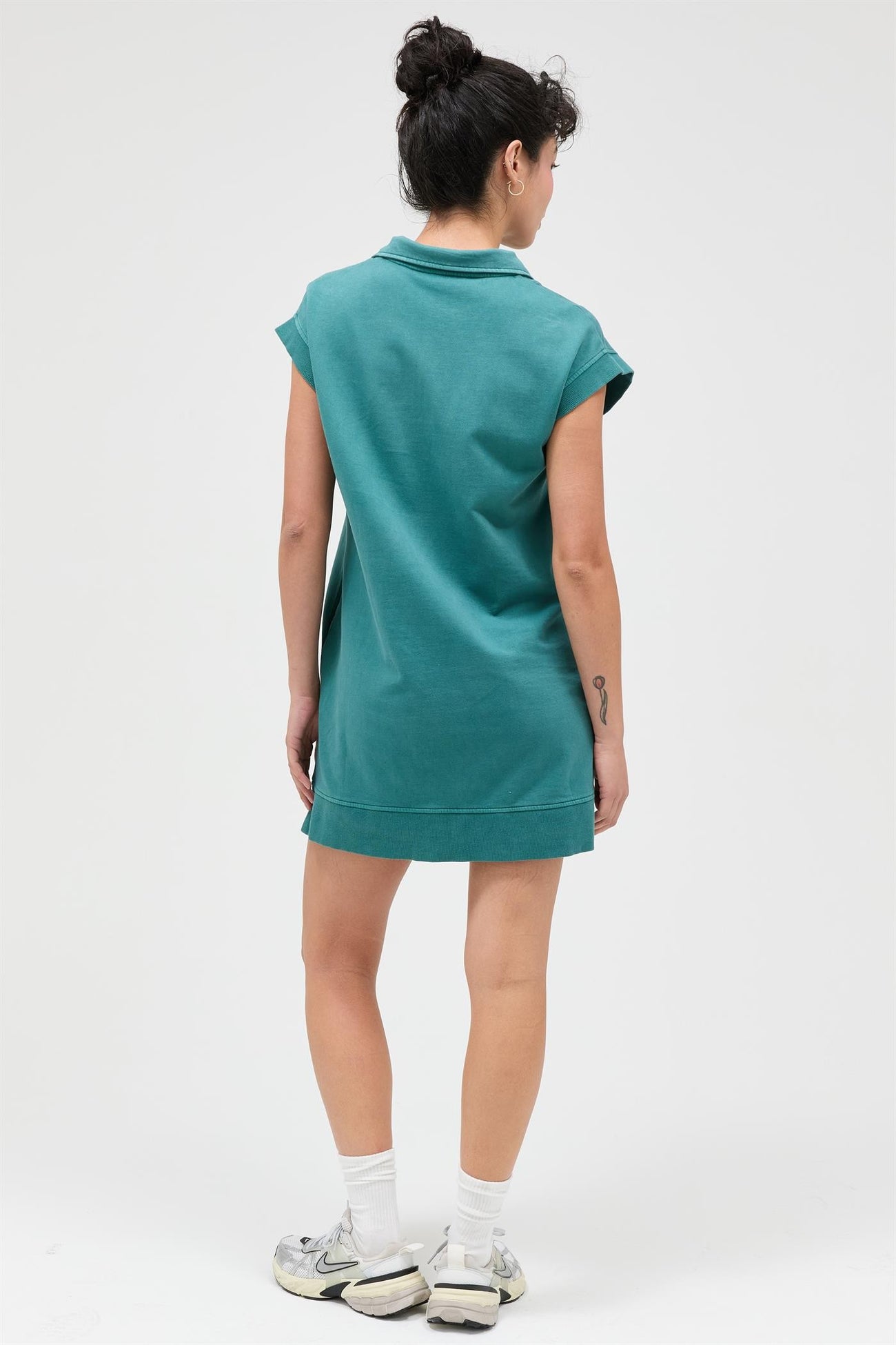 woman wearing a short teal polo dress with cap sleeves, viewed from the back
