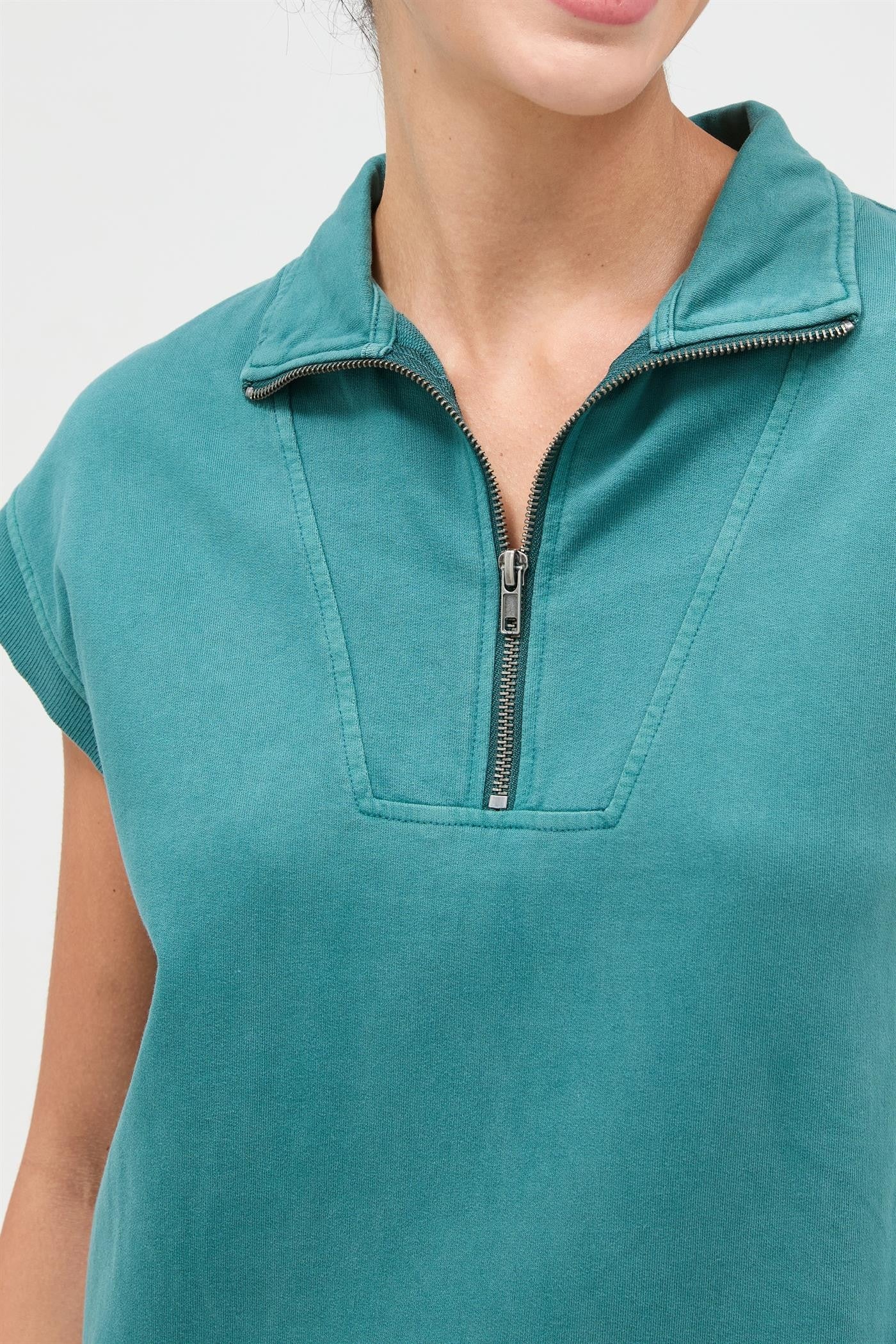 woman wearing a teal zip-up collared short sleeve top with a relaxed fit