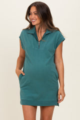 woman wearing a teal maternity dress with a zip neckline and short sleeves, featuring pockets