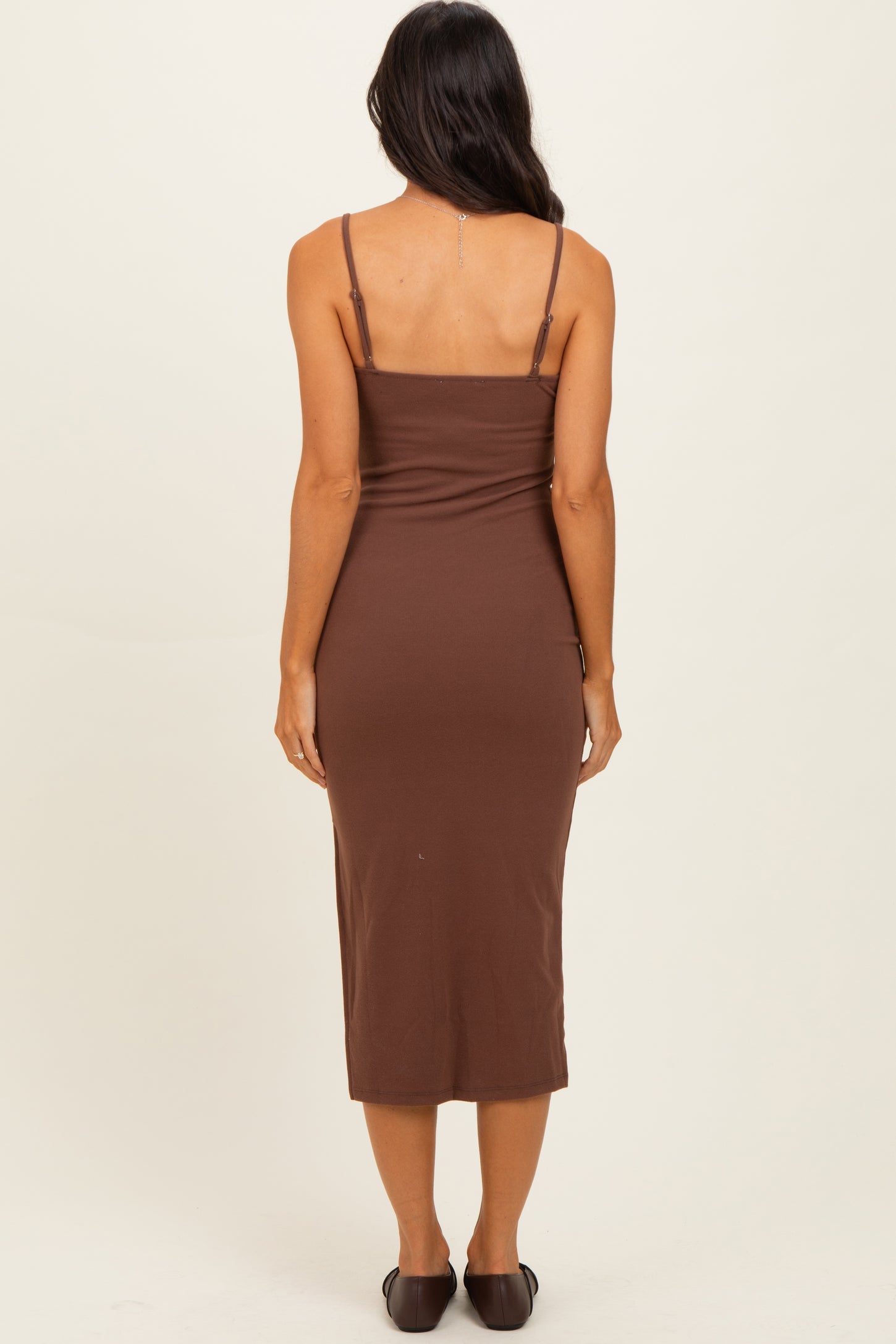 woman wearing a fitted brown midi dress with adjustable spaghetti straps and a sleek silhouette