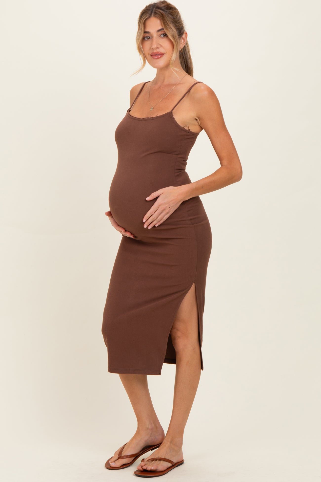 woman wearing a brown maternity dress with side slits and holding her baby bump
