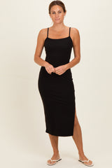 woman wearing a black maxi dress with thin straps and a side slit, styled with flat sandals