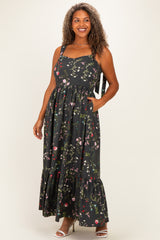woman wearing a black floral plus size maxi dress with a square neckline and pockets, standing and smiling