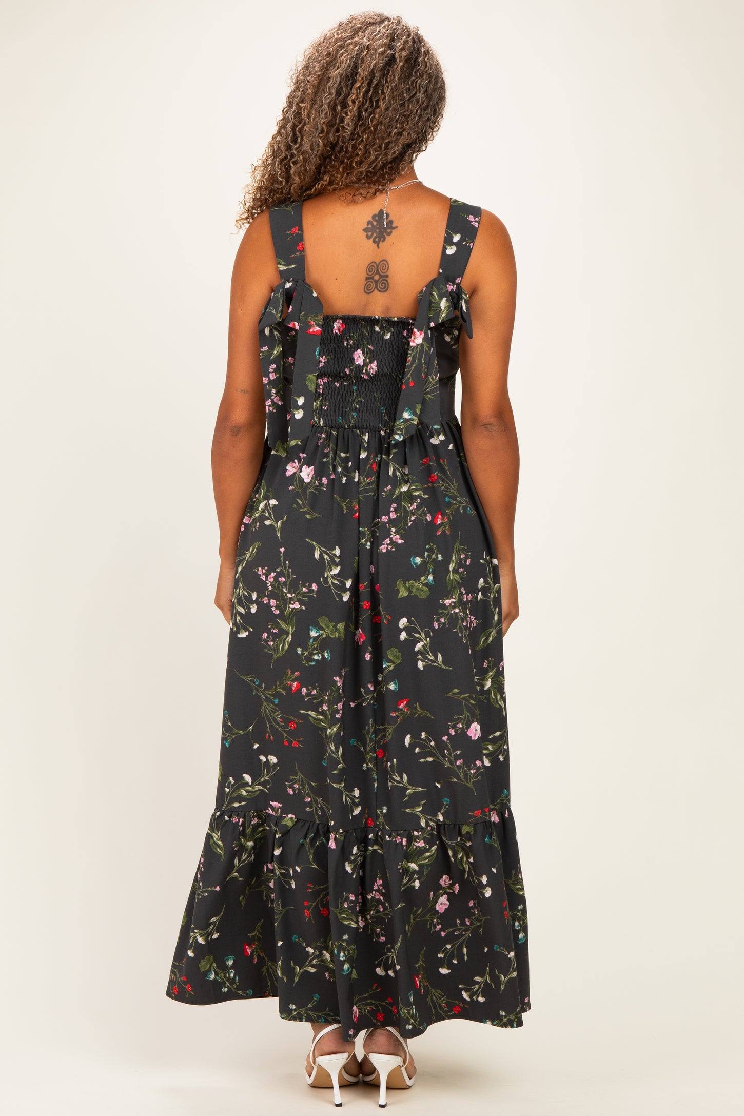 woman wearing a black floral plus size maxi dress with a smocked back and ruffled straps, viewed from the back