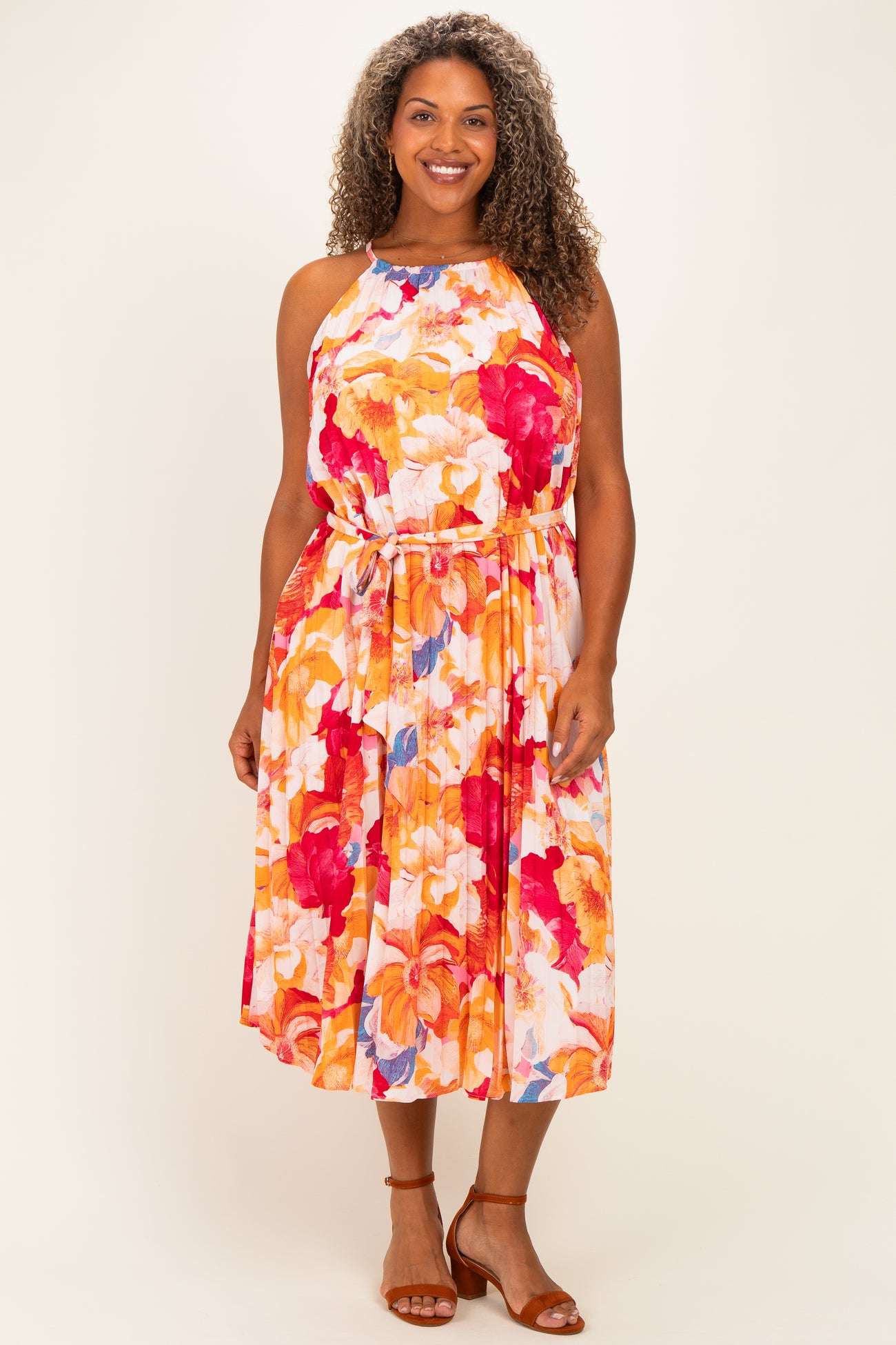 woman wearing a colorful floral plus-size dress with a halter neckline and tie waist, standing with a smile